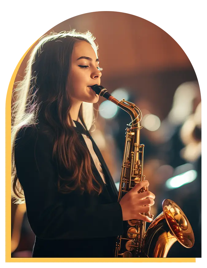 A young woman with long brown hair plays a saxophone, wearing a dark blazer. She stands in a softly lit room, likely at a concert or music lessons Westchase, with blurred figures and warm lighting in the background.