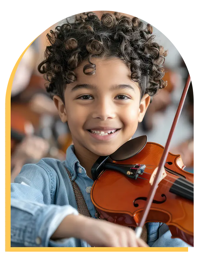 A young child with curly hair smiles while playing a violin, wearing a denim shirt. The softly blurred background highlights the child’s joyful expression and the instrument—capturing the delight found in music lessons Westchase offers.