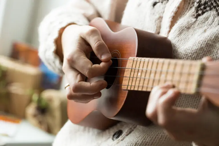 A close-up of a person wearing a sweater playing a wooden ukulele, with their fingers strumming the strings and background softly out of focus—capturing the joy inspired by Music Lessons in Lehi.