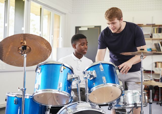 male-pupil-with-teacher-playing-drums-in-music-lesson.jpg